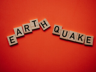 Obraz premium Inscription earthquake from vibration moves on background. Concept of earthquake, destruction and shifts of earth's crust. Wooden square blocks with letters are laid out on orange sheet. Slow motion