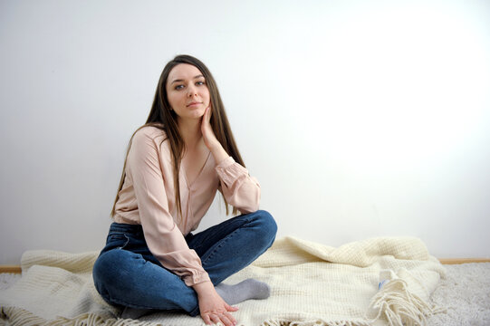 a girl in jeans and a pink blouse sits on the floor on a plaid looks into the frame long hair on a white background calm look in a bright room. High quality photo
