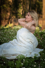 Portrait of a young beautiful fair-haired girl in a white veil in the forest on a meadow with flowers.