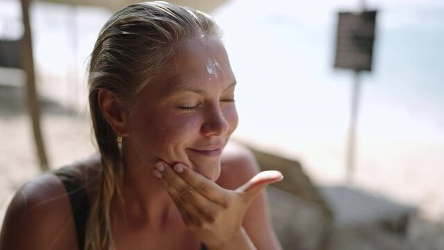 Blonde caucasian female surfer applying sunscreen on her face. Tanned young surfing woman putting spf on her cheeks, nose and forehead close-up. Portrait of surfer girl usinf spf skin protection