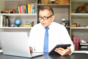 Gerente en la oficina, consultando información en su computadora y tableta.