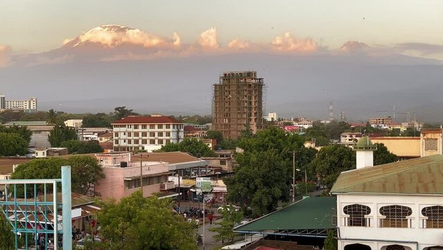 Moshi East African town street traffic with cars, rickshaws and local people daily routine with a huge and  magnificent Kilimanjaro mountain 5895m covered with ice and snows landscape view. Tanzania.
