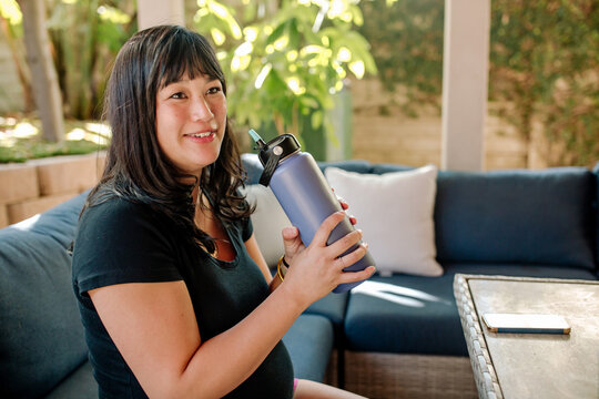 smiling pregnant woman sitting on couch and drinking from water bottle