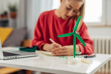 Closeup view of a windmill model and a teenage girl studying behind