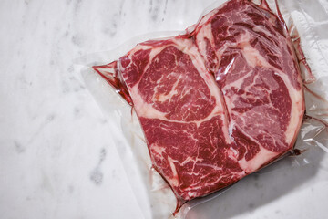 Vacuum packed meats. Raw beef steaks on white marble background, top view. Copy space.