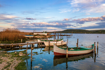 The tranquil afternoon on a lake with a wooden pier and boats in the colorful sky.