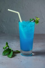 Healthy Blue Lagoon Mojito soda served in glass with straw side view on grey background