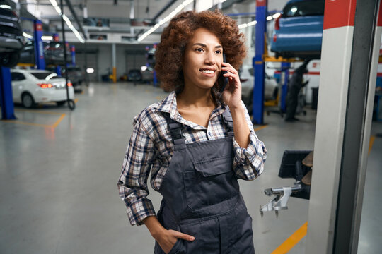 Woman auto mechanic in car repair shop talking on mobile phone