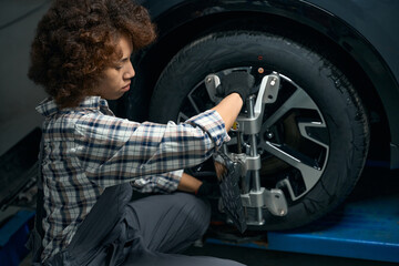 Obraz na płótnie Canvas Young woman adjusts wheel alignment in auto repair shop