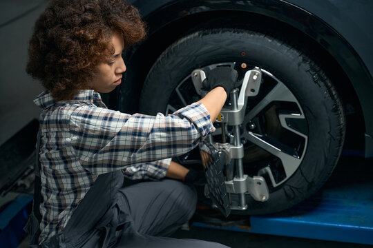 Young woman adjusts wheel alignment in auto repair shop - Powered by Adobe