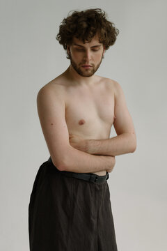 A handsome guy with pierced nipples and curvy hair looks thoughtfully 