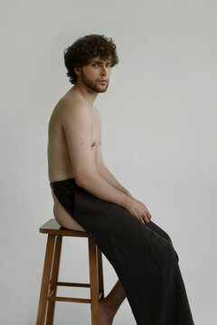 A bearded guy sits on a chair in a trousers that covers his front side