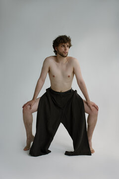 A curly bearded guy stays topless in a black trousers on his toes