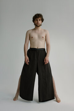 A curly bearded guy stays on his toes topless in a black trousers 