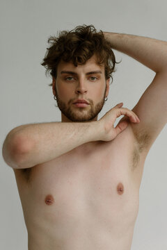 A handsome guy with pierced nipples and curvy hair looks thoughtfully 