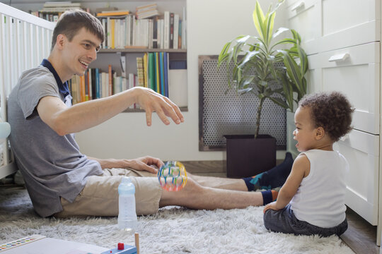 father playing with child baby toddler at home, showing toy ball