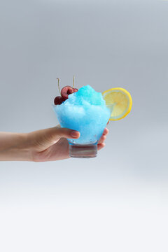 Blue summer slushie with cherry and lemon in hand
