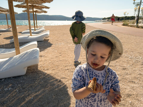 A child on the beach is messing up with the ice cream 