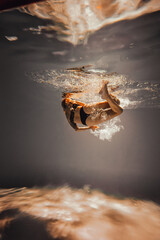Art work. A slender, tanned girl with an athletic figure and blond hair, in black lingerie, dives and spins underwater in the pool. Aesthetic image for your design or decoration.