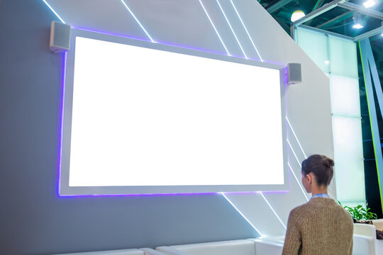 Mockup image: woman looking at blank large white interactive wall display at modern technology exhibition, museum, trade show. Mock up, white screen, copyspace, template, education concept