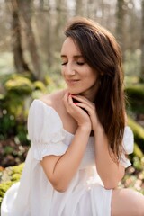 Portrait of a woman in the forest. She is sitting in a white dress on a meadow with snowdrops in a spring forest