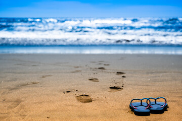 Fototapeta na wymiar Blue Sandals on Beach with Fine-Grained Sand