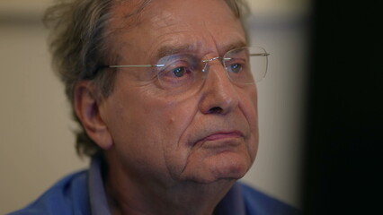 Senior man reading content online in front of computer screen. One mature older male 70s person browsing internet closeup face