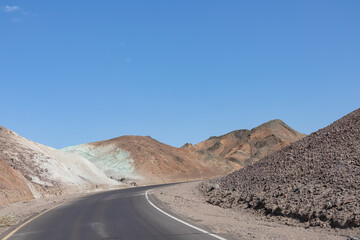 Panoramic view of endless empty road leading to colorful geology of multi hued Artist Palette rock formations in Death Valley National Park near Furnace Creek, California, USA. Black mountains