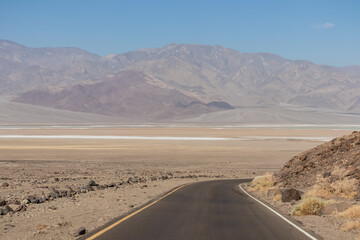 Panoramic view of endless empty road leading to colorful geology of multi hued Artist Palette rock formations in Death Valley National Park near Furnace Creek, California, USA. Black mountains