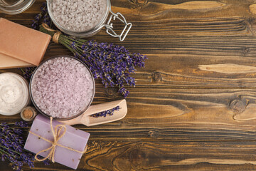 Fototapeta na wymiar Lavender spa. Essential oils, sea salt, handmade soap, cream and body scrub with lavender flowers on brown texture wood. Natural herbal cosmetics with flowers and lavender aroma.Aromatherapy and relax