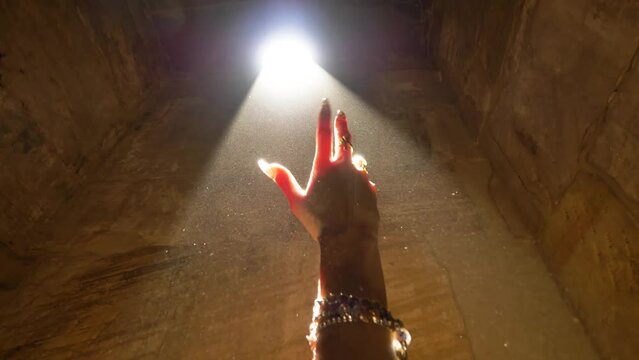 2022 - Close-up of a dancer's hand, long fingernails and jewelry in a shaft of sunlight coming through Egypt's Karnak Temple Complex.