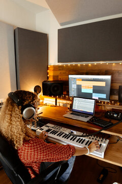 Music producer at home studio using keyboard controller from the back