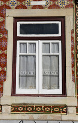 Fototapeta na wymiar White wooden window with curtain on tiled facade