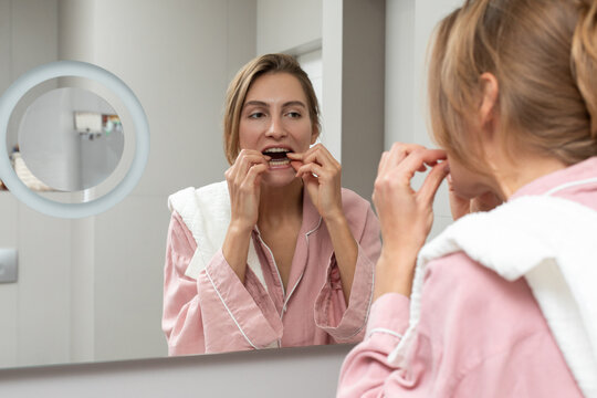 White woman using dental floss in bathroom