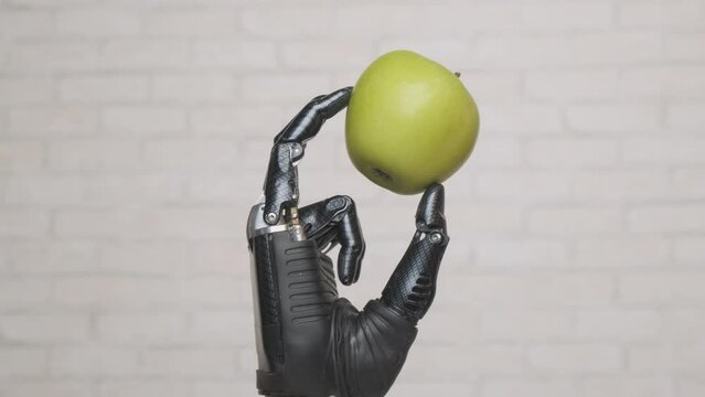 Artificial robotic hand takes green apple and holds it with his fingers.