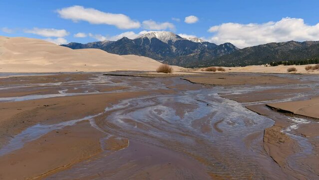 Spring Medano Creek - A sunny Spring day view of Medano Creek, with white clouds flying over rolling Great Sand Dunes and snow-capped Mt. Herard in background. Great Sand Dunes National Park, CO, USA.
