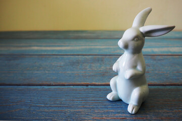 a ceramic figurine of a light blue Easter bunny stands on a blue wooden background, side view. the...