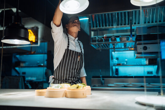 Male chef adjusting lamp over table - Powered by Adobe