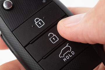 Unlocking a car with button on the keychain. Man's hand holds car key on white background close up.