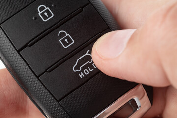Open the trunk of a car with button on the keychain. man's hand holds car key on white background close up.