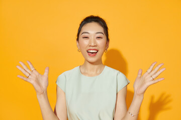 Surprised happy asian woman looking at the camera over yellow