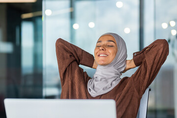 Business woman in hijab resting, Arab woman in hijab with her hands behind her head and smiling with closed eyes, woman in glasses dreaming about future results, good achievements and success.