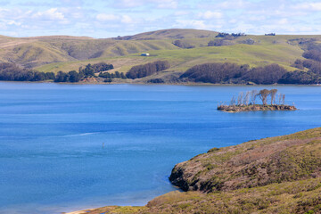 Small island in blue waters and rolling green hills on California coast