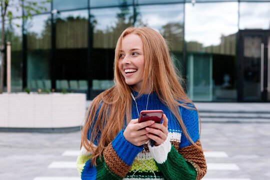 Cheerful red head woman using smartphone on street