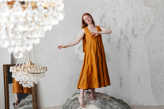 Dancing woman in dress standing on stone in studio with chandelier