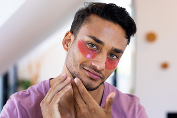 Smiling biracial man with eye masks inspecting his face in bathroom mirror - Powered by Adobe