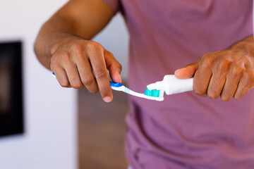 Midsection of biracial man putting toothpaste on toothbrush in bathroom