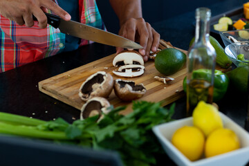 Close up of hands of biracial man preparing dinner, chopping mushrooms in kitchen