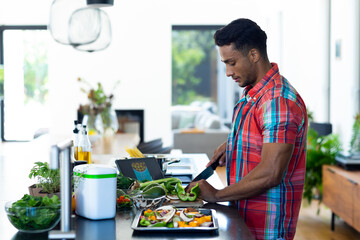 Happy biracial man preparing dinner, chopping vegetables in kitchen