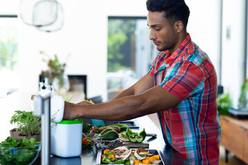 Happy biracial man preparing dinner, chopping vegetables and composting waste in kitchen